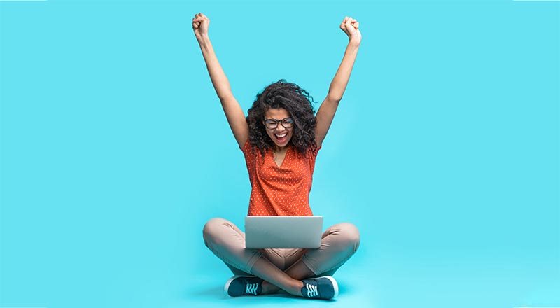 Woman sitting on the ground with a laptop and arms in the air