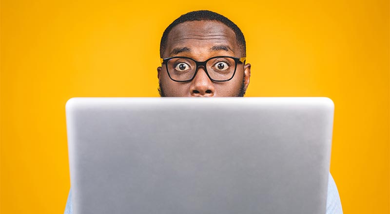 Man with glasses looking surprised behind his computer screen